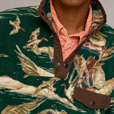 A person wearing a green fleece pullover with a duck hunting pattern, over a peach-colored collared shirt.
