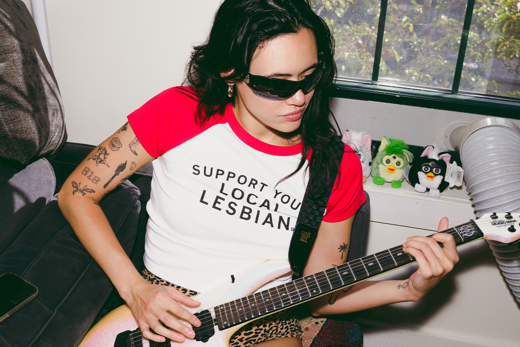 rivkah reyes wearing sunglasses playing a guitar with furbies in the background