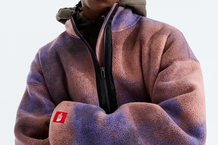 Person wearing a pink and purple tie-dye fleece jacket with a black zipper and a red North Face patch on the sleeve.