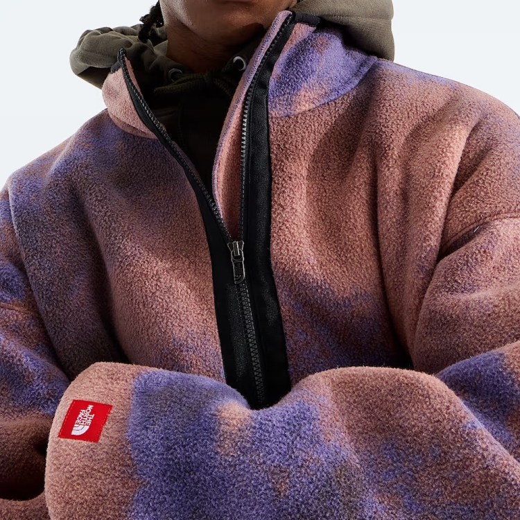 Person wearing a pink and purple tie-dye fleece jacket with a black zipper and a red North Face patch on the sleeve.