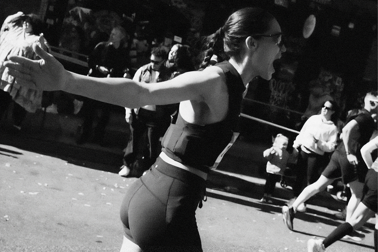 Black and white photo of a woman in athletic wear, mid-stride, with her mouth open and arm outstretched.