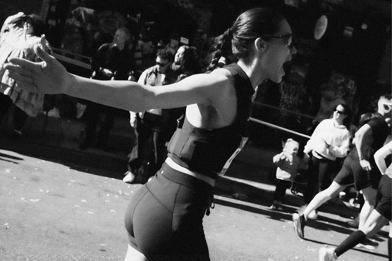 Black and white photo of a woman in athletic wear, mid-stride, with her mouth open and arm outstretched.