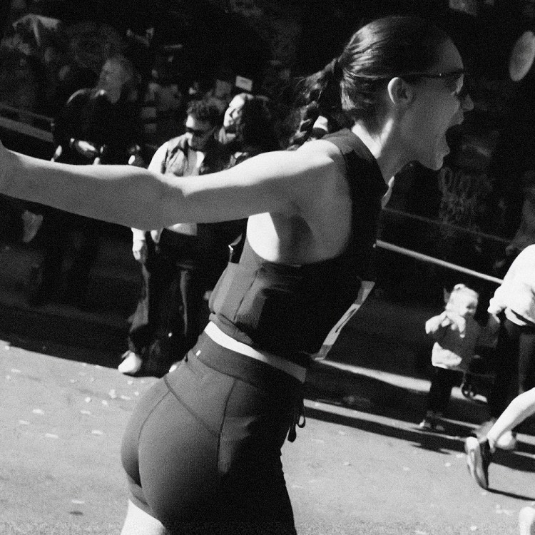 Black and white photo of a woman in athletic wear, mid-stride, with her mouth open and arm outstretched.