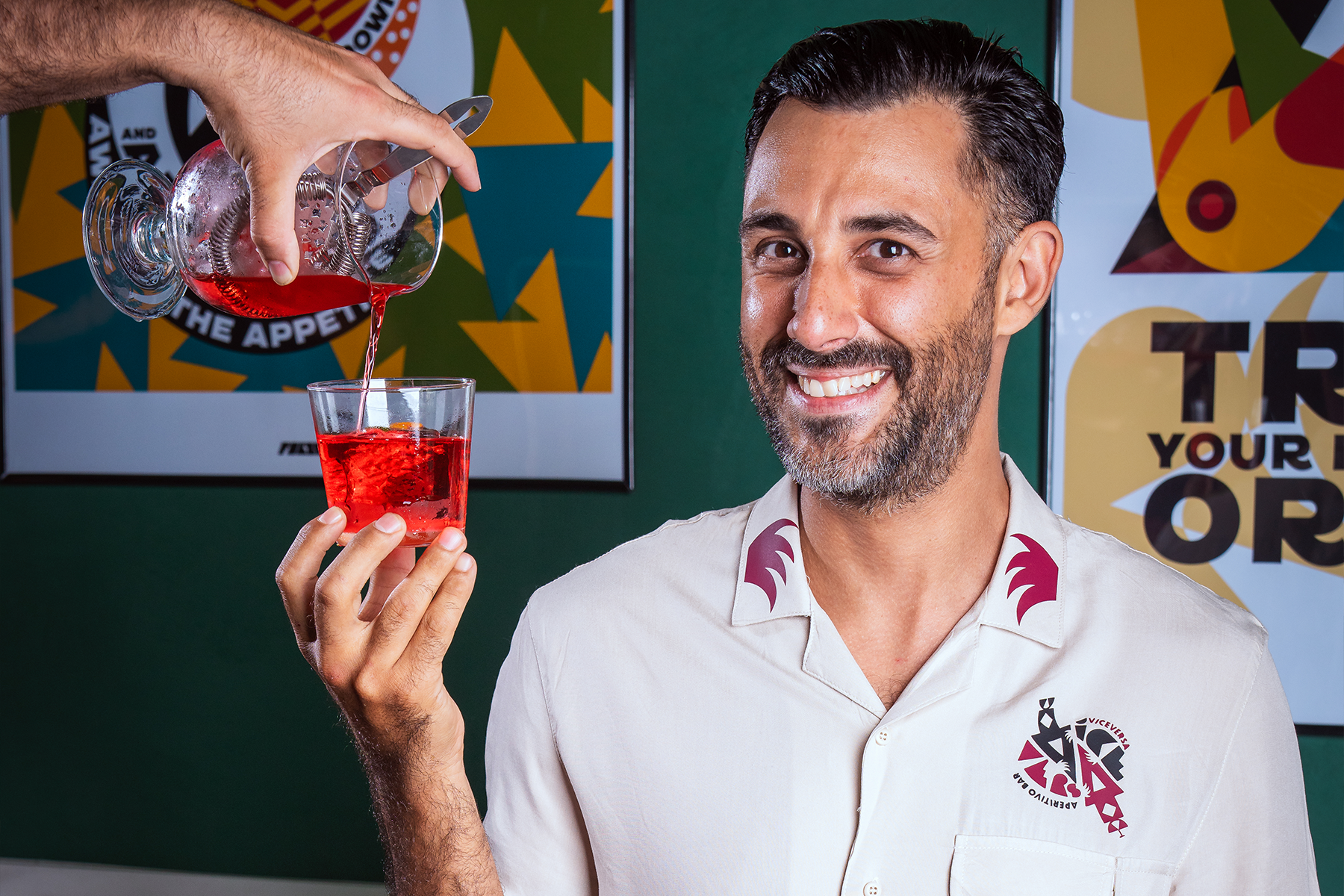 a man with a short beard and dark hair in a white shirt holding a negroni