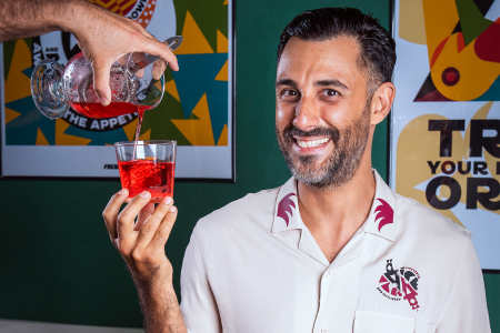 a man with a short beard and dark hair in a white shirt holding a negroni