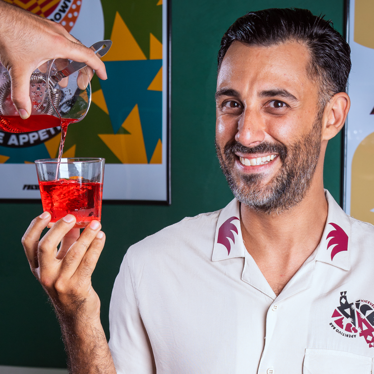 a man with a short beard and dark hair in a white shirt holding a negroni