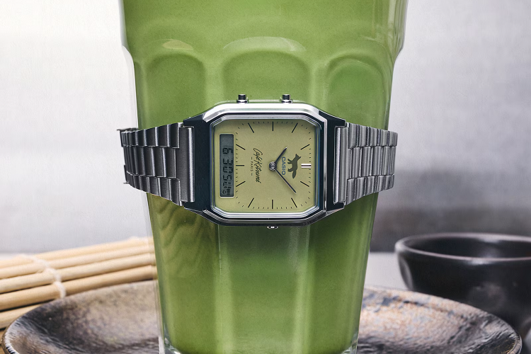 Silver Casio watch with a green face and fox logo, wrapped around a glass of green matcha tea.