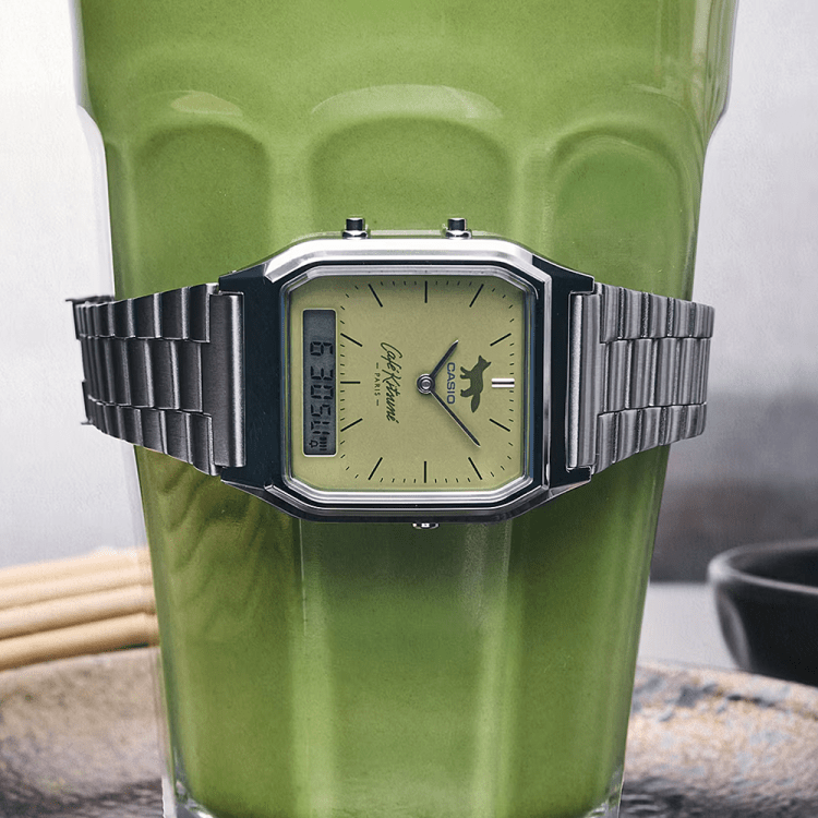 Silver Casio watch with a green face and fox logo, wrapped around a glass of green matcha tea.