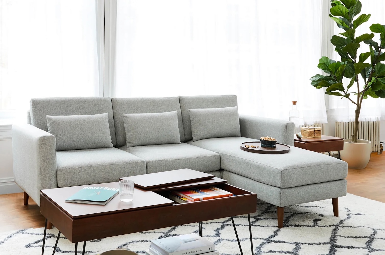 Light gray sectional sofa with a chaise lounge, a dark wood coffee table with storage, and a fiddle-leaf fig plant