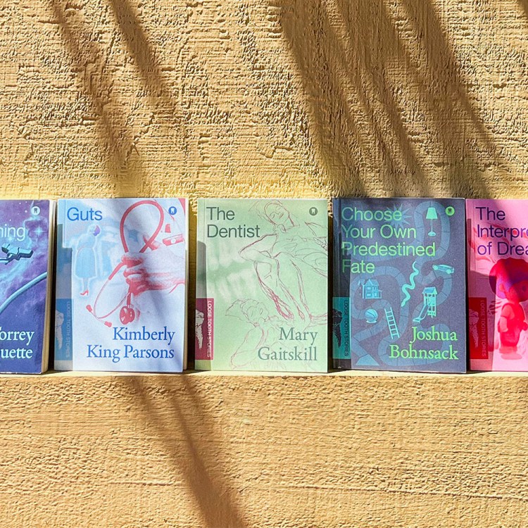 Five books with colorful, illustrated covers stand upright against a textured yellow wall, casting shadows.