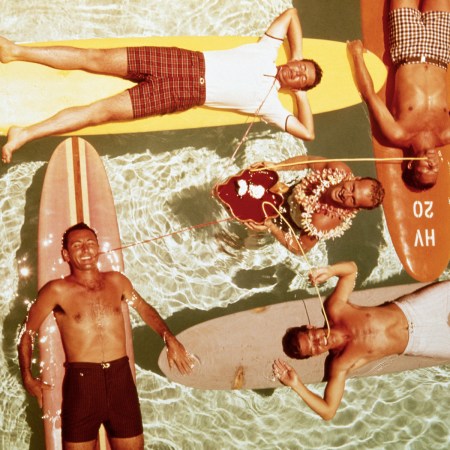 Overhead view of five men on surfboards in a pool, some drinking from straws, one wearing a lei.