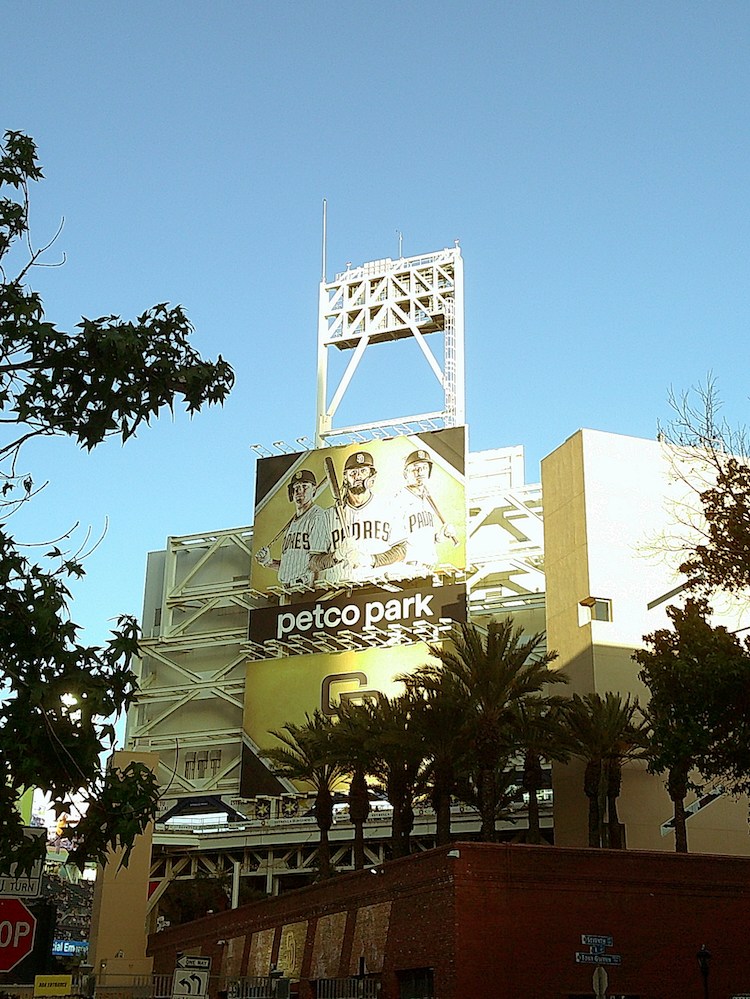 Petco Park stadium with a large billboard of three baseball players and "petco park" sign, palm trees.
