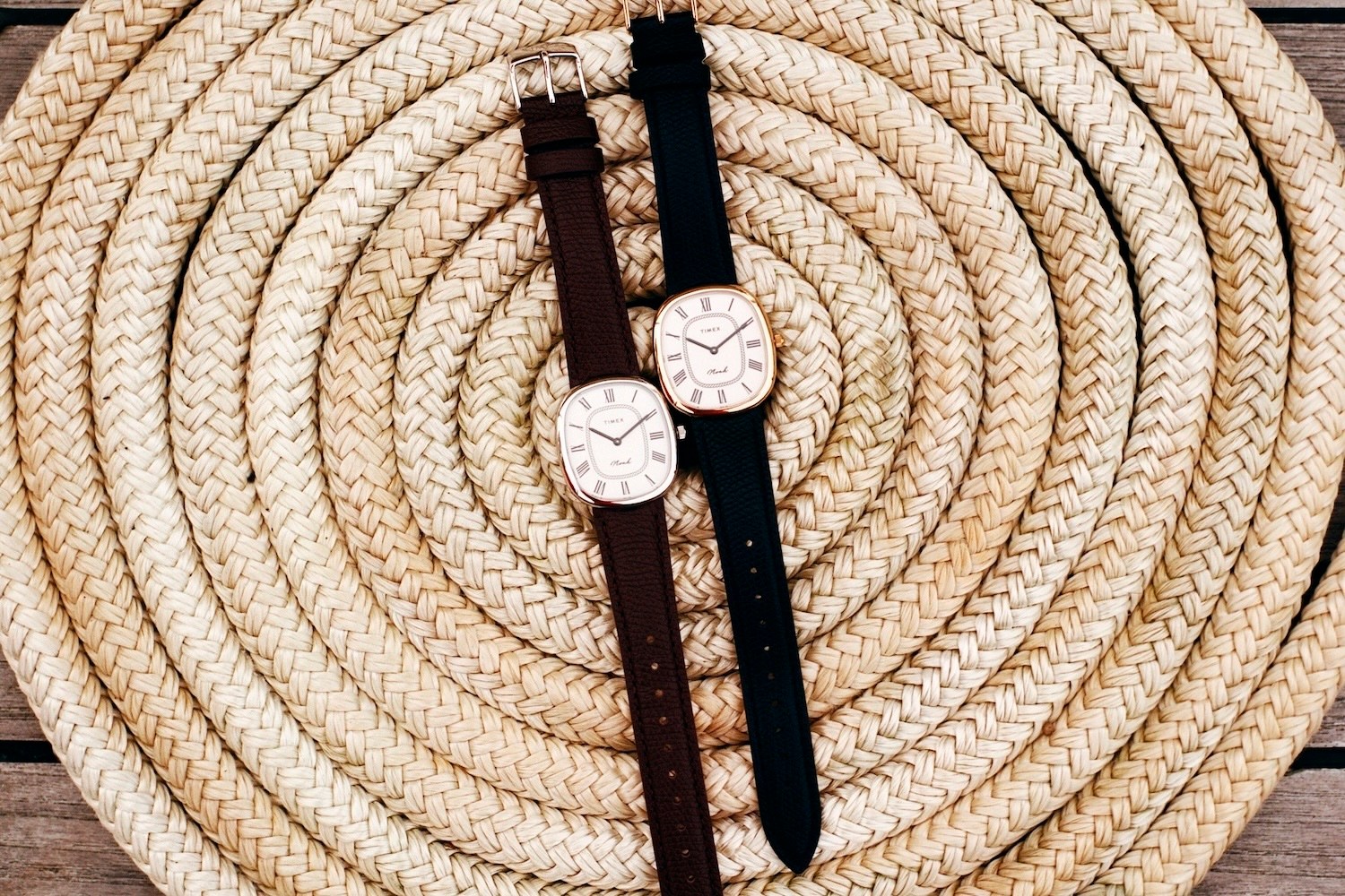 Two oval-faced Timex watches with Roman numerals, one with a brown band and one with a black band, on coiled rope.