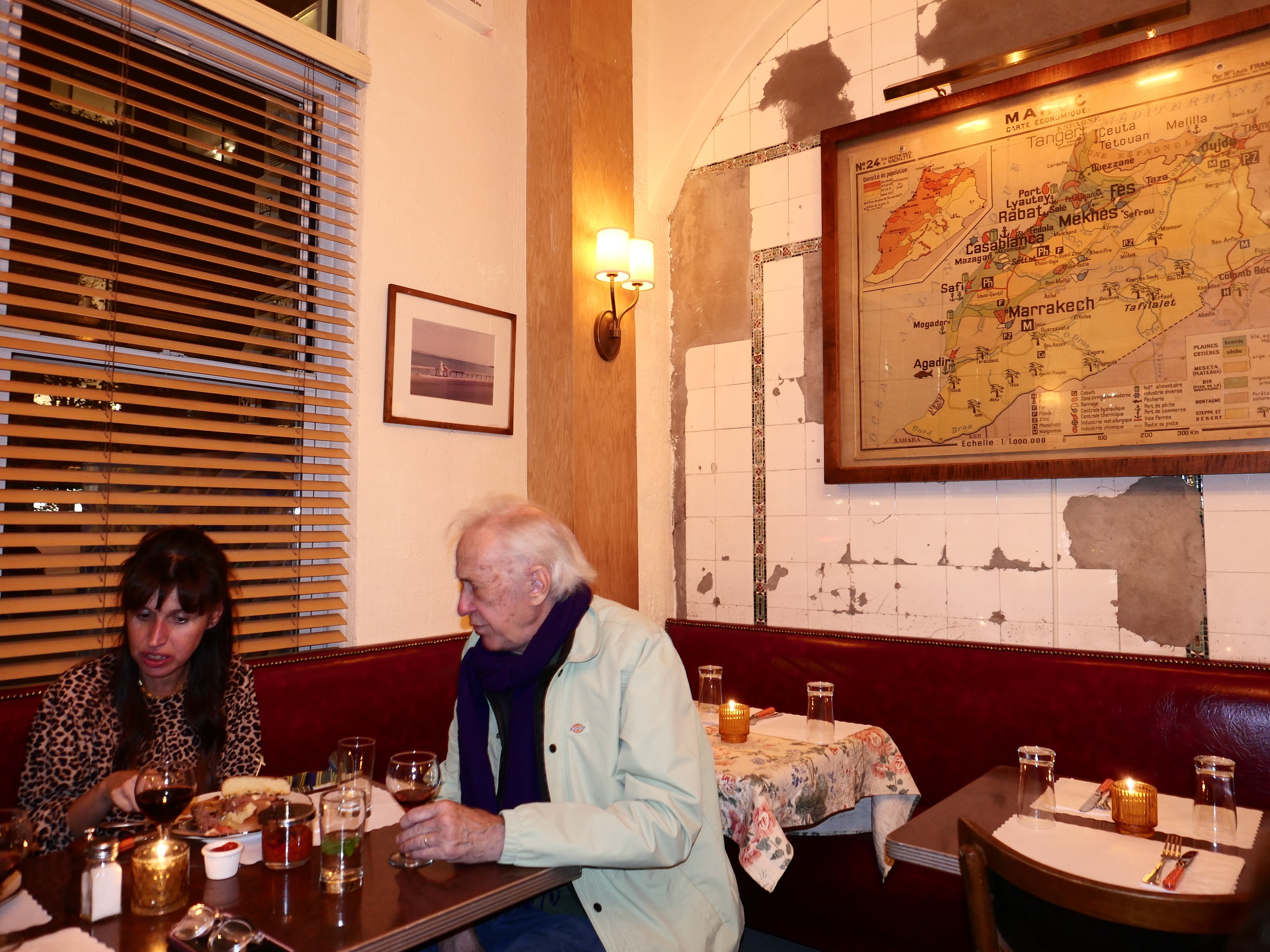 A woman in a leopard print top converses with an older man at a cozy restaurant table, surrounded by warm lighting and decor.