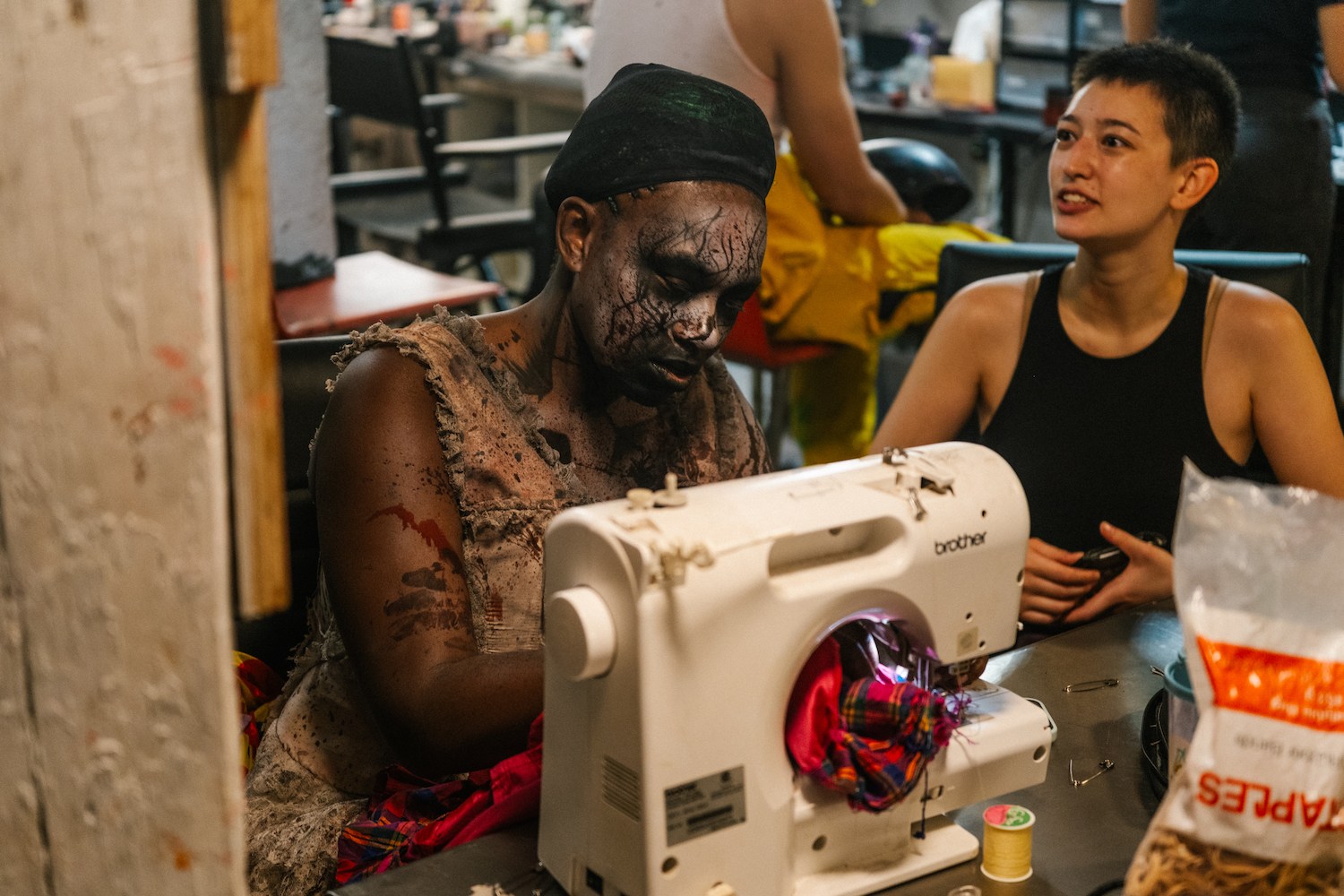 a woman in bloody makeup sitting at a sewing machine