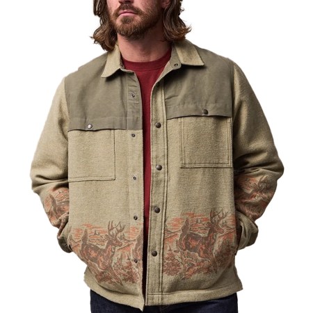 Man in a beige and olive green jacket with a deer and forest pattern along the bottom and sleeves.