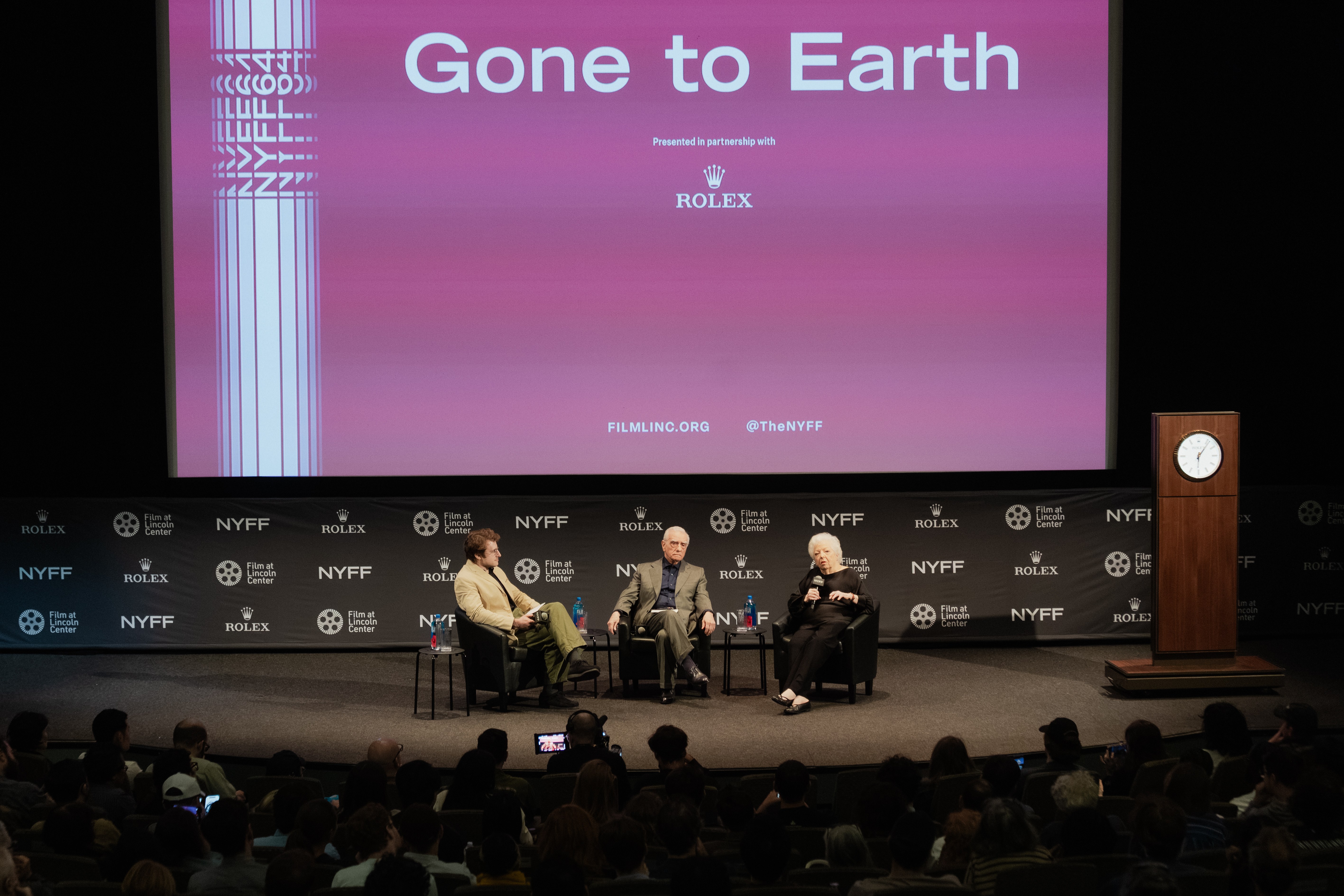 Panel discussion titled "Gone to Earth" with three speakers on stage, audience visible in a theater setting.