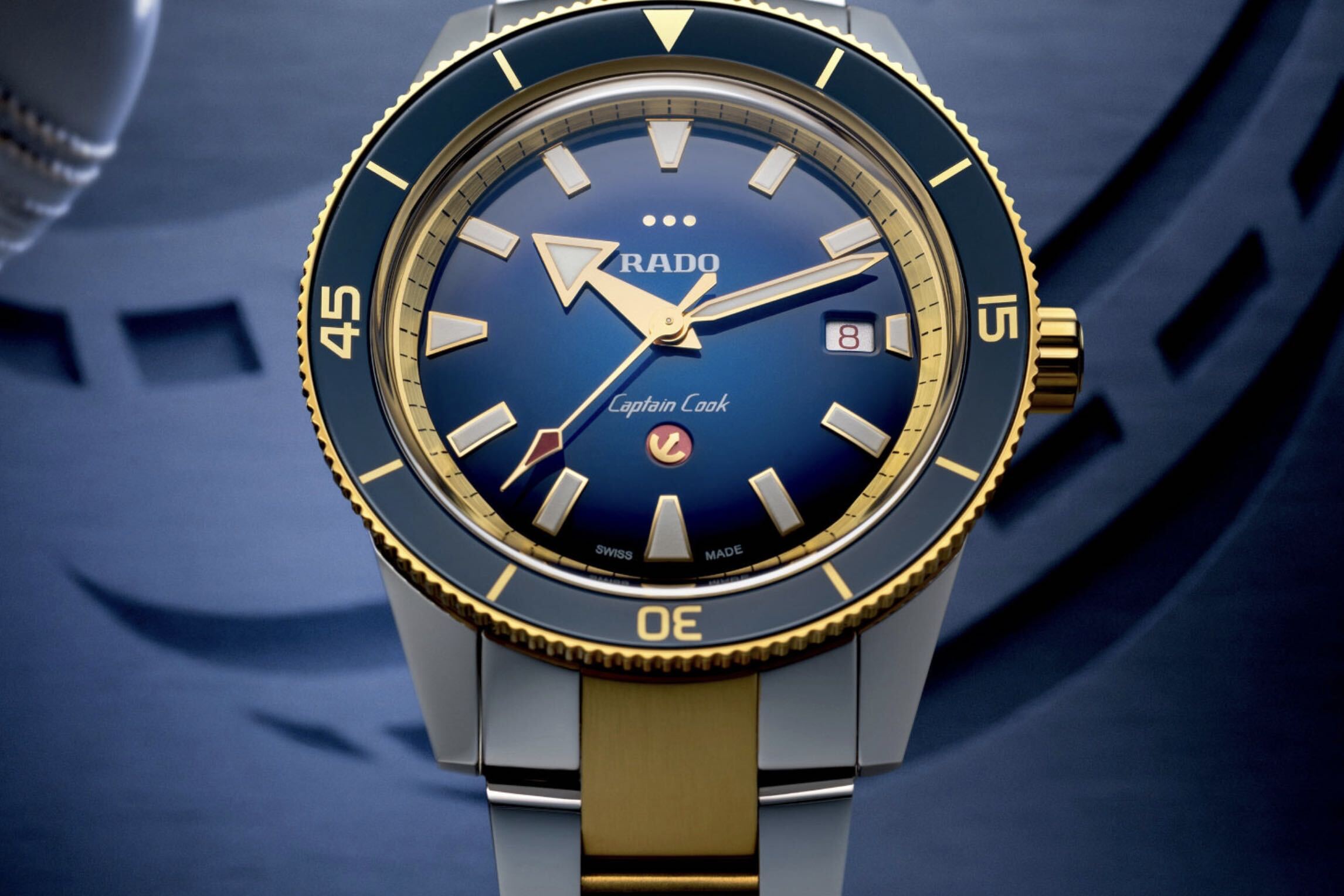Close-up of a Rado Captain Cook watch with a blue dial, gold hands, and a two-tone gold and silver band.