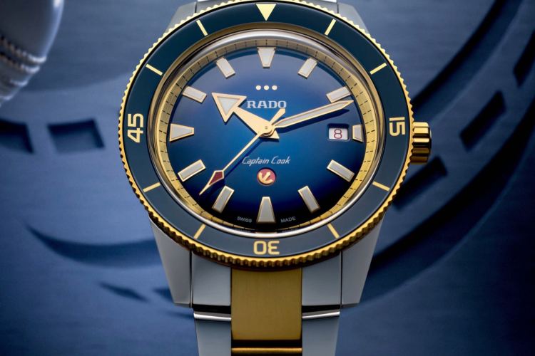 Close-up of a Rado Captain Cook watch with a blue dial, gold hands, and a two-tone gold and silver band.