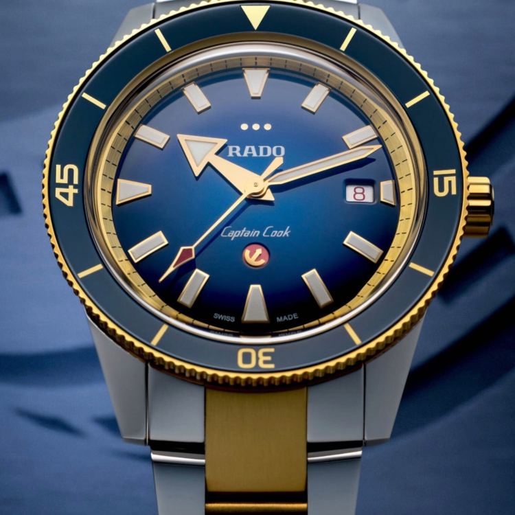 Close-up of a Rado Captain Cook watch with a blue dial, gold hands, and a two-tone gold and silver band.