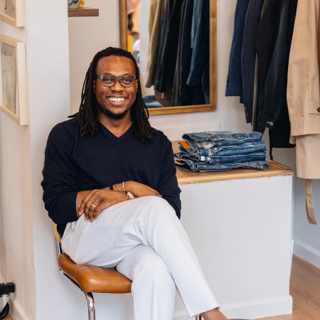 Daniel Dele-Tunji, wearing a navy sweater and white pants, sitting in a clothing store.