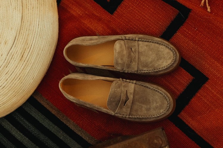 Pair of gray suede loafers with tan interiors on a red, black, and white patterned rug