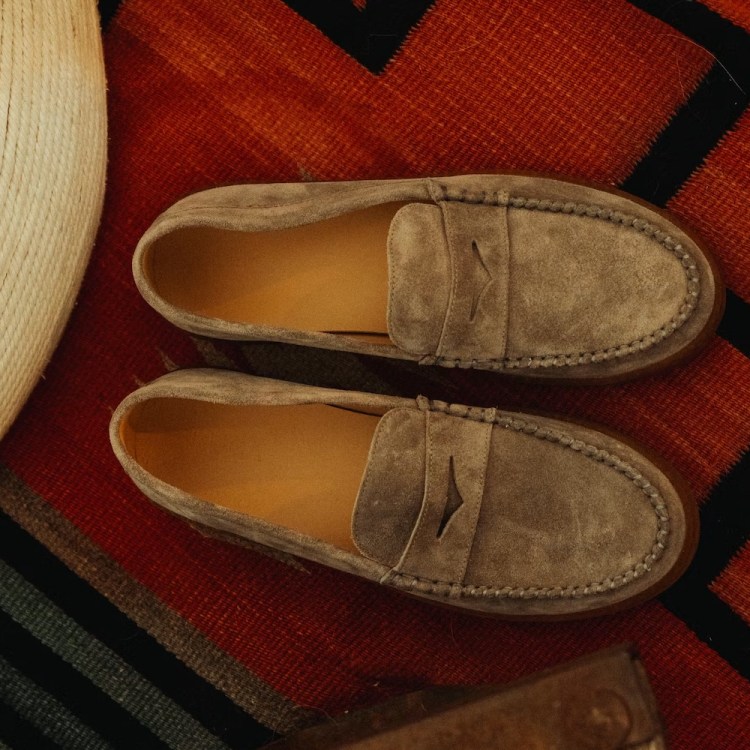 Pair of gray suede loafers with tan interiors on a red, black, and white patterned rug