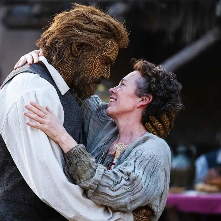 A woman with curly hair smiles up at a man with a hairy, woven face, embracing him.