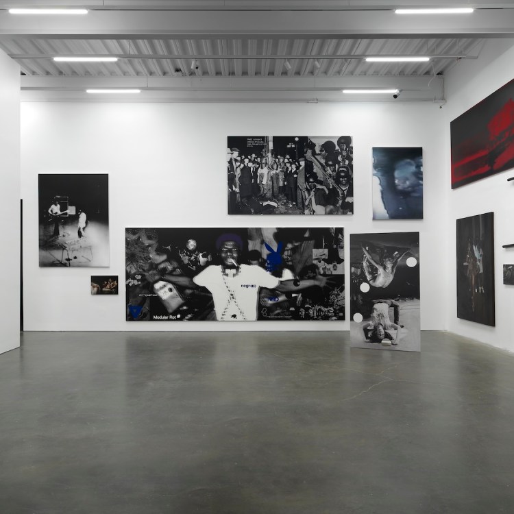Art gallery with large black and white photographs, a red abstract painting, and black pipe sculptures on white walls.