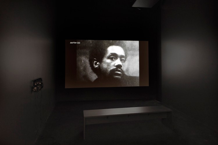 Photo of a Black man in a dark room with a bench and headphones