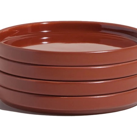 Stack of four glossy, rust-colored ceramic plates with raised edges, casting a shadow on a white background.