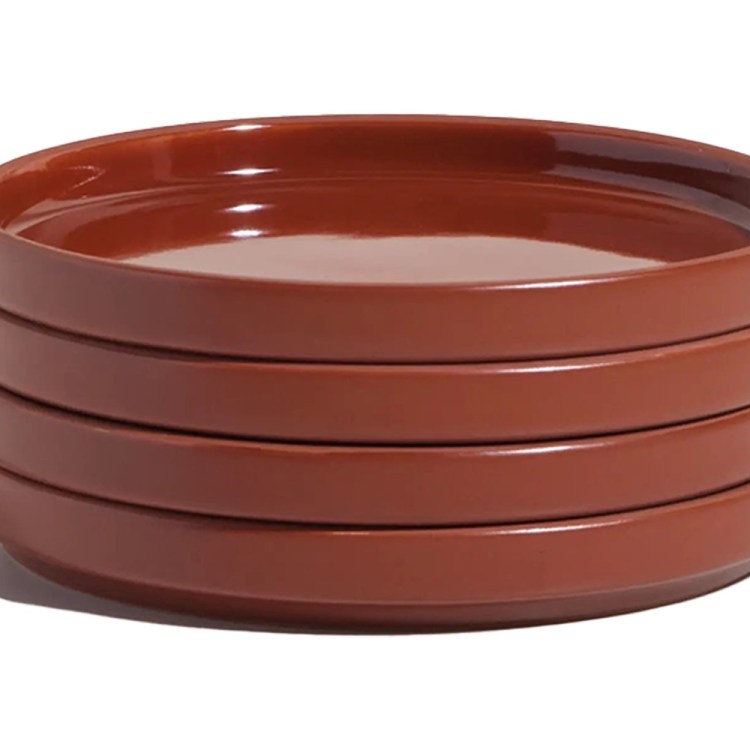 Stack of four glossy, rust-colored ceramic plates with raised edges, casting a shadow on a white background.