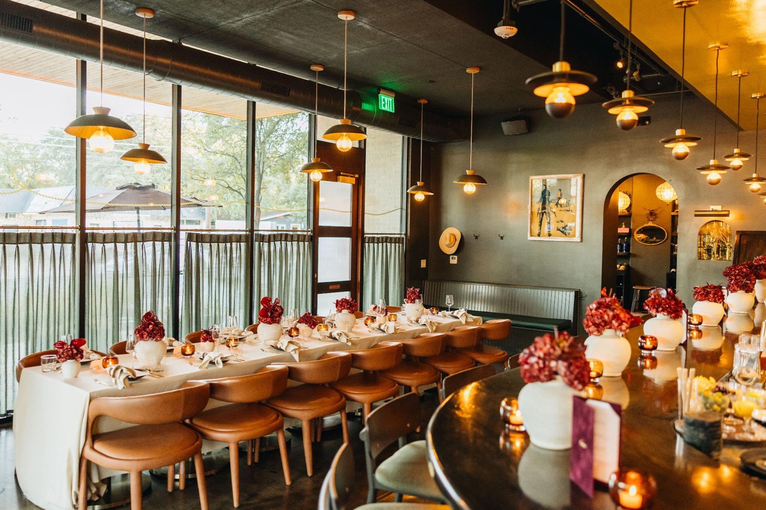 A long dining table set with white tablecloths and red floral centerpieces, next to a bar with more flowers.