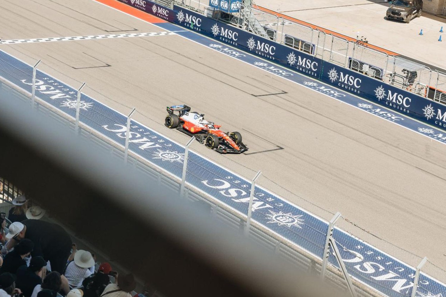 An orange and white Formula 1 race car speeds down a track lined with "MSC Cruises" banners and fences.