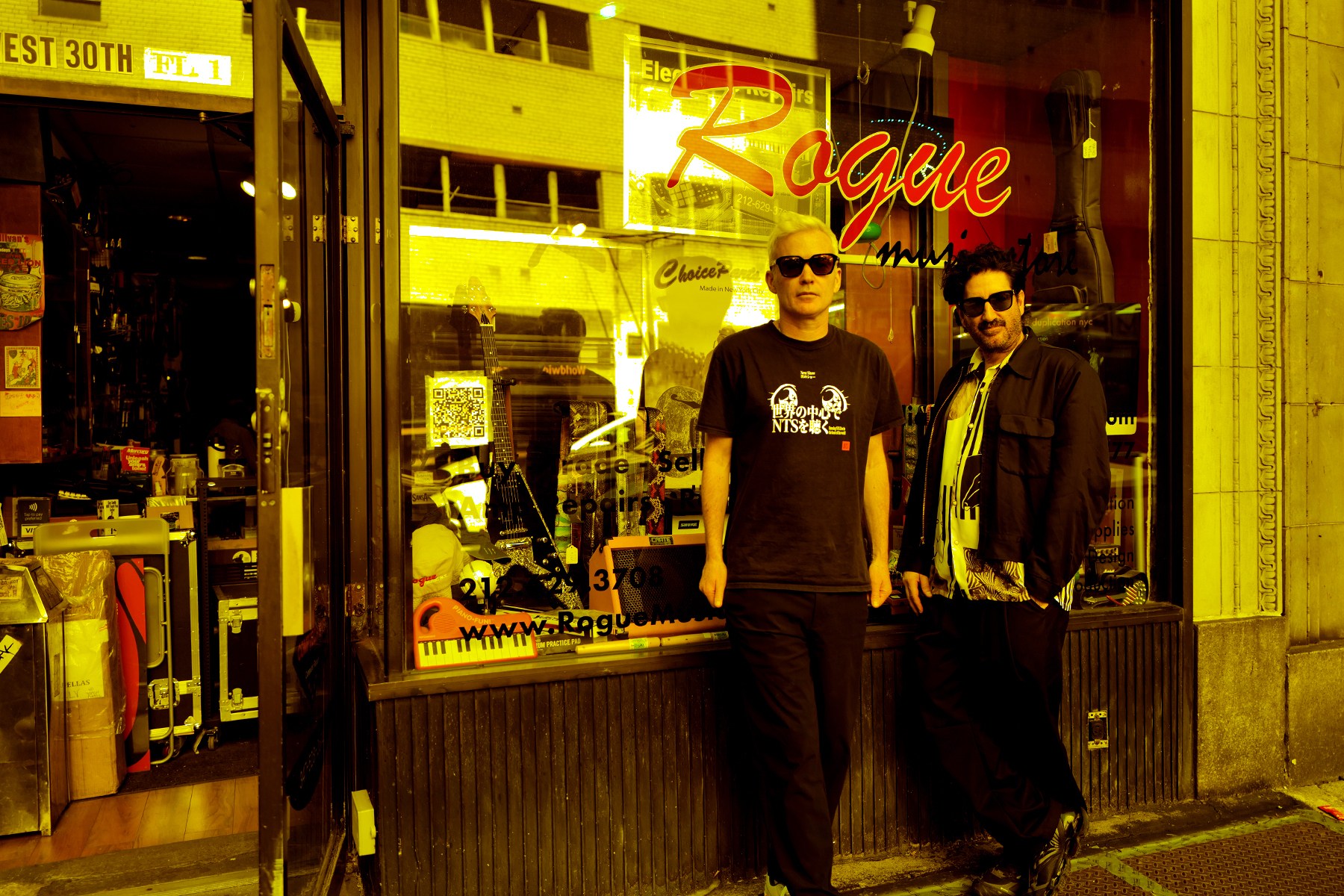 Two men in sunglasses stand outside a music store with "Rogue" in red neon on the window.
