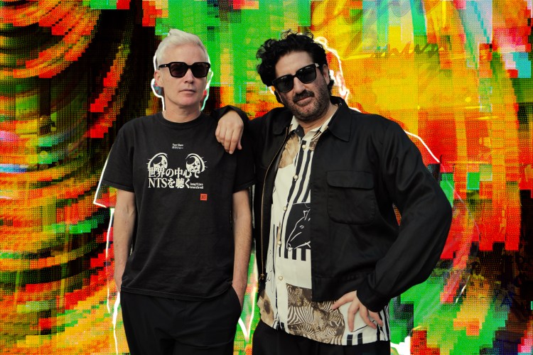 Two men in sunglasses, one with white hair and one with a beard, pose against a vibrant, glitchy background.
