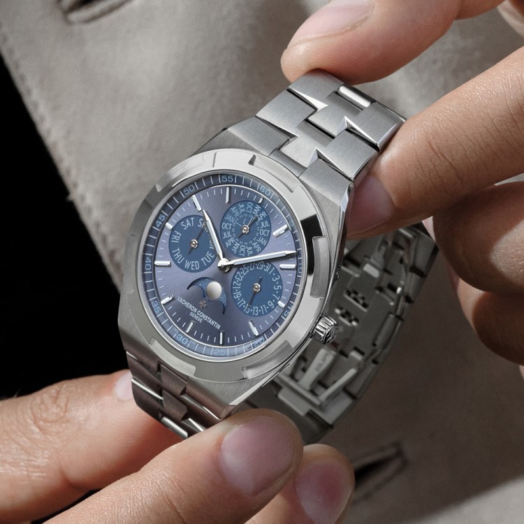 Hands adjust a Vacheron Constantin Overseas Perpetual Calendar Ultra-Thin watch with a blue dial and steel bracelet.
