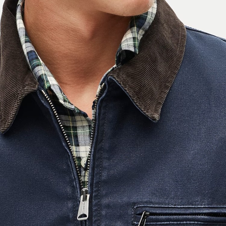 Close-up of a person wearing a navy blue jacket with a brown corduroy collar over a green and white plaid shirt.