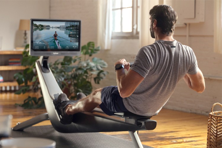 Man rowing on an exercise machine, watching a video of a person rowing on a lake on the attached screen.