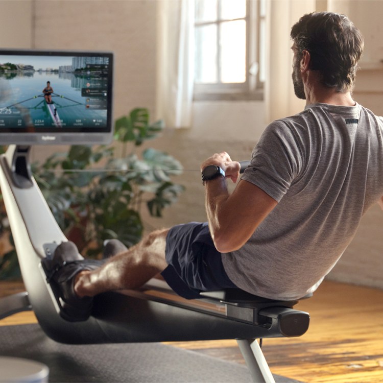 Man rowing on an exercise machine, watching a video of a person rowing on a lake on the attached screen.
