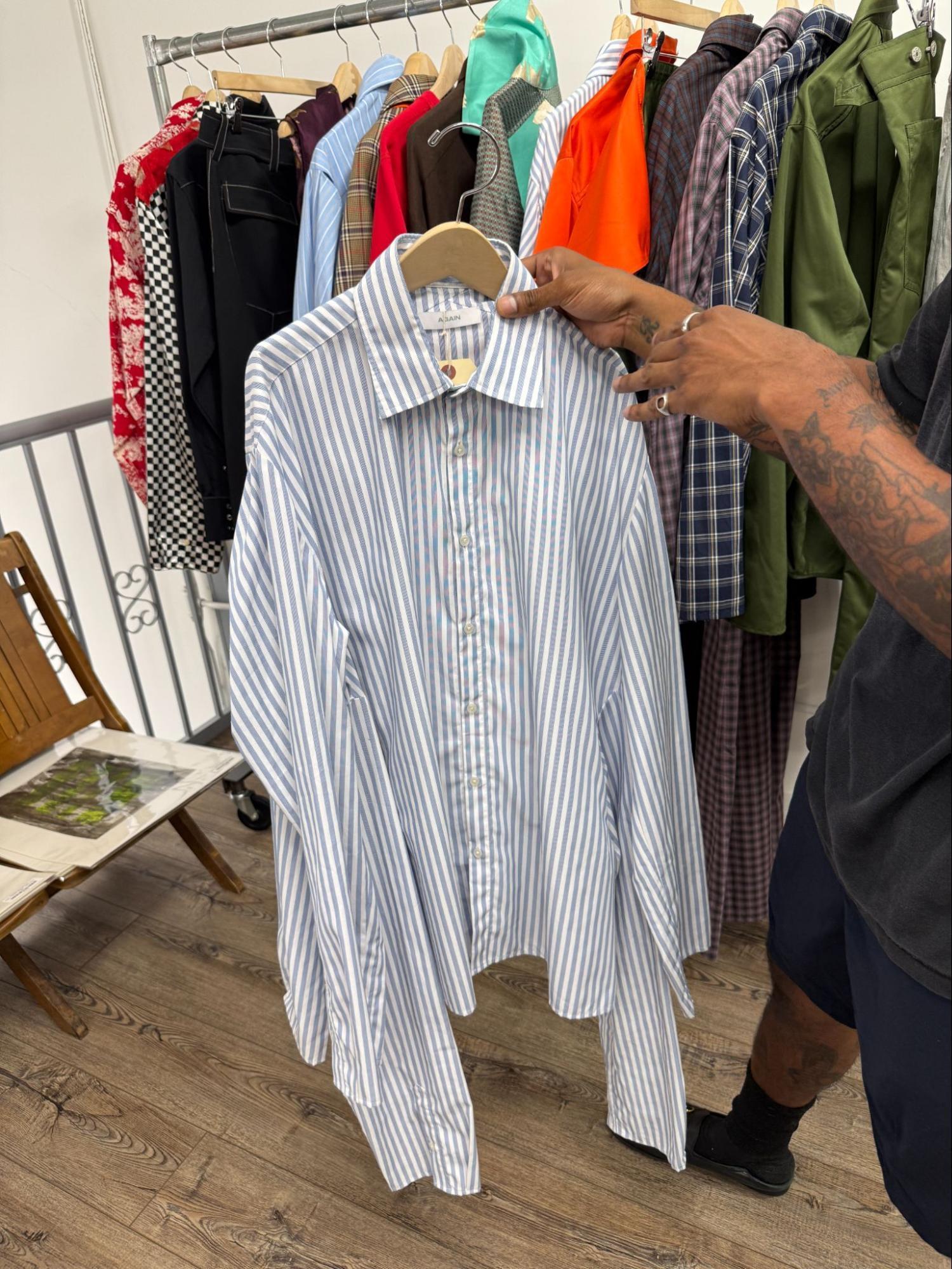 A person holds a blue and white striped shirt in front of a rack of various colorful clothing items.