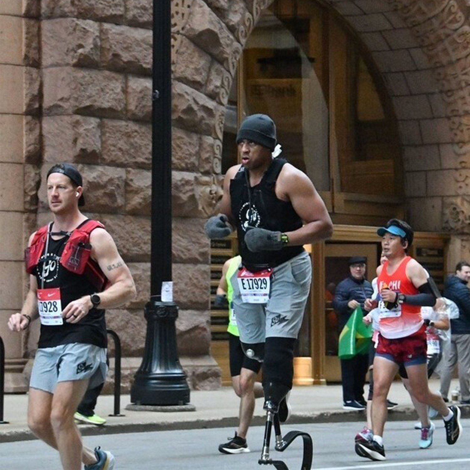 A man with a prosthetic running blade on his right leg runs a marathon, alongside other runners.