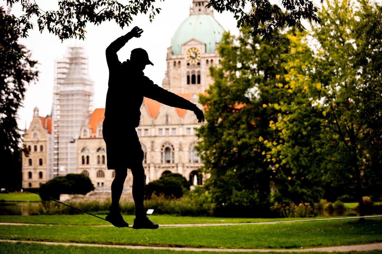 Silhouette of a person slacklining in a park with a large domed building in the background.
