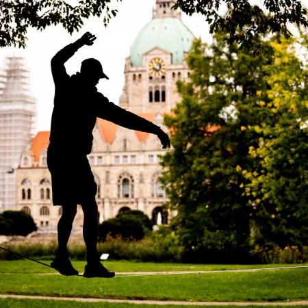Silhouette of a person slacklining in a park with a large domed building in the background.