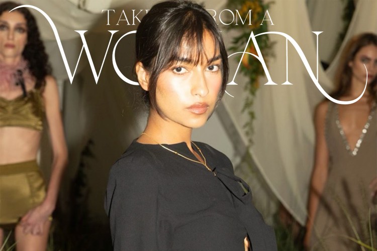 A woman with dark hair and bangs in a black top looks at the viewer, with two blurred models behind her.