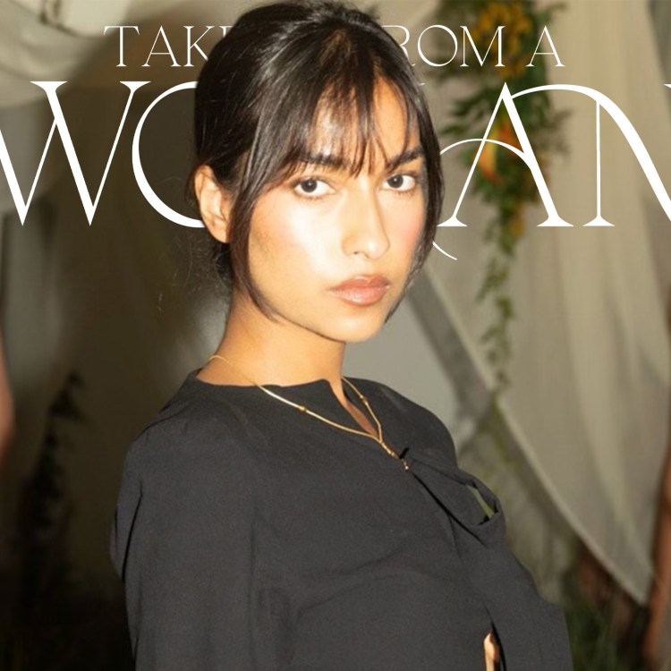 A woman with dark hair and bangs in a black top looks at the viewer, with two blurred models behind her.
